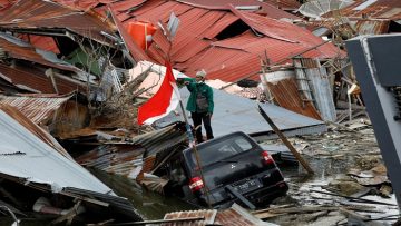 A man gestures towards a search and rescue team while looking for victims in the earthquake and liquefaction affected Balaroa neighbourhood in Palu